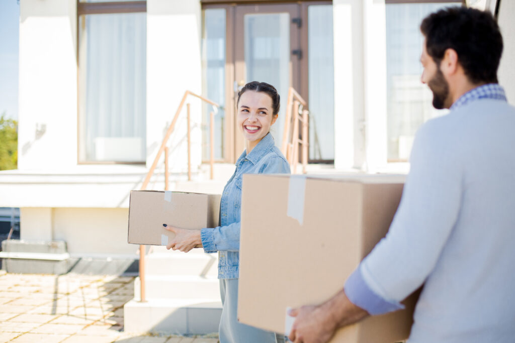 Happy young woman with box talking to her husband while helping to relocate